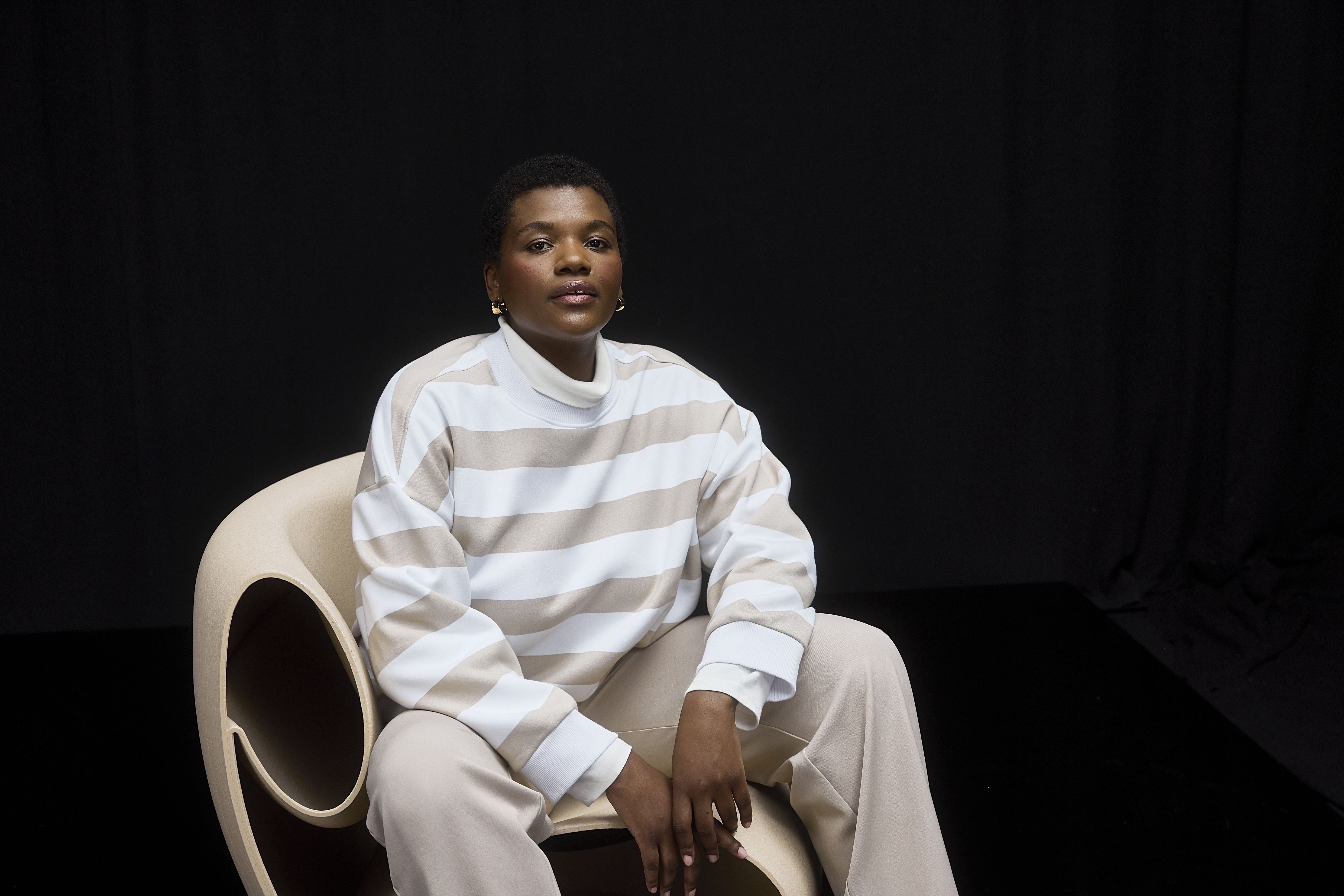 Frau sitzt, trägt beige-weiß gestreiftes Sweatshirt, beige Hose und weiße Turnschuhe