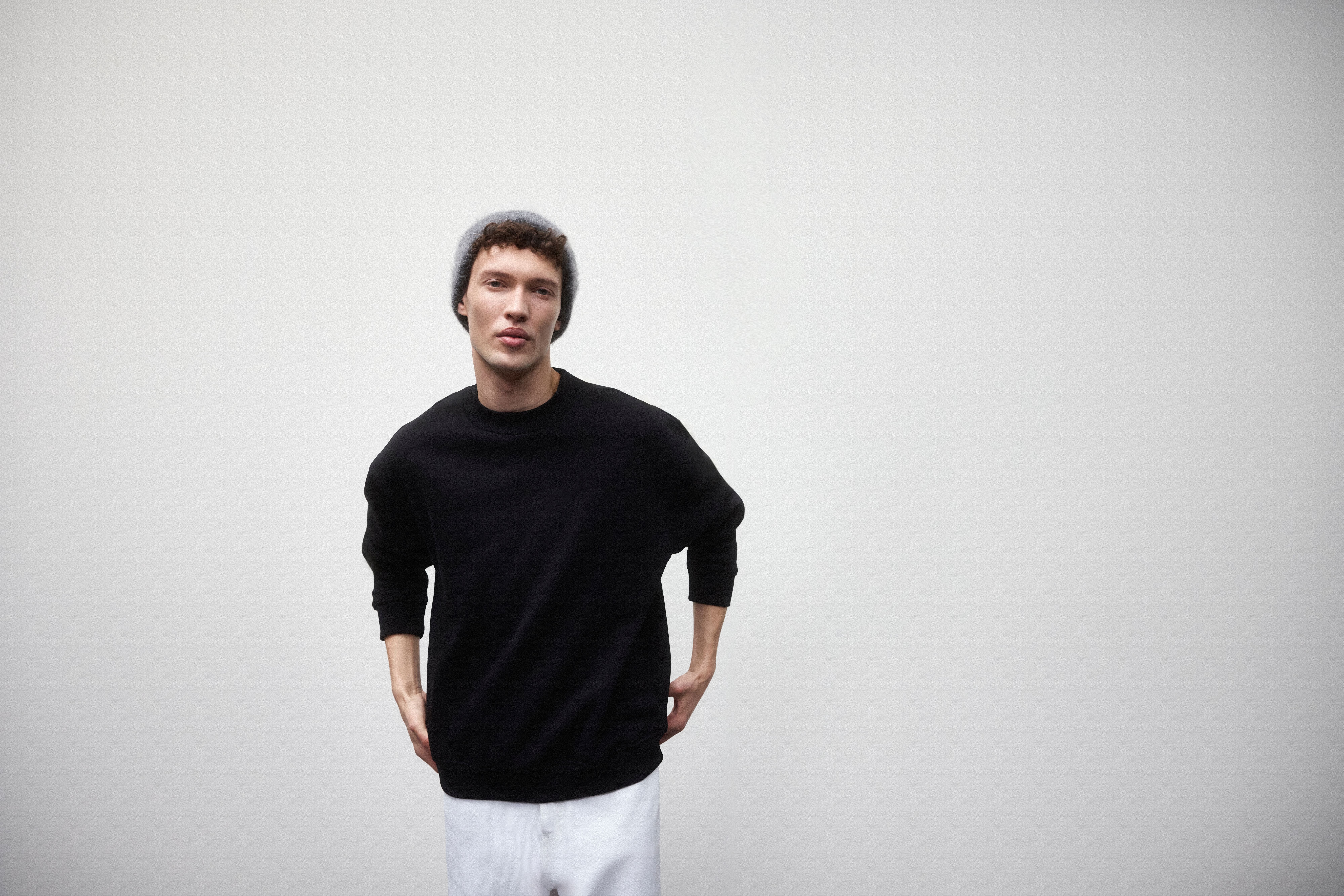 Mann trägt schwarzes Sweatshirt, mit weißer Jeans und grauer Mütze